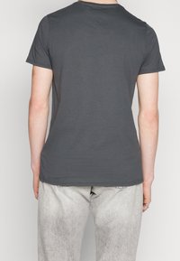 Graues Kurzarm-T-Shirt aus Baumwolle mit Rundhalsausschnitt und glatter Textur. Getragen mit hellen, verblassten Hosen.