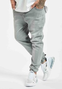 Joggers ajustados de color gris claro con cinturilla elástica, acompañados de zapatillas de malla blancas con una suela de aire transparente y acentos negros.