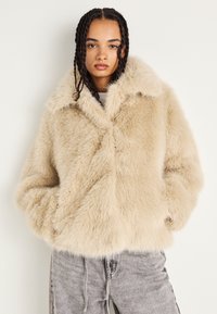 Lys beige faux fur-jakke med bred krage, myk tekstur og løs passform. Har sidelommer og kryss-frontdesign.