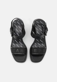 Paire de sandales noires à bout ouvert avec brides à la cheville et brides avant embossées formant le mot "Pepe Jeans" sur fond blanc.