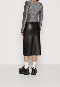 Svart läder midi kjol med en elegant design, kombinerad med en åtsittande långärmad topp i silverglitter och kraftiga svarta sneakers.