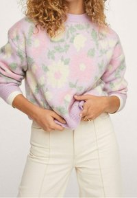 Pull de couleur pastel en lavande avec des motifs floraux verts et jaunes. Texture douce, coupe courte, associé à un pantalon couleur crème.