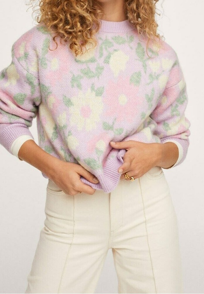 Pull de couleur pastel en lavande avec des motifs floraux verts et jaunes. Texture douce, coupe courte, associé à un pantalon couleur crème.