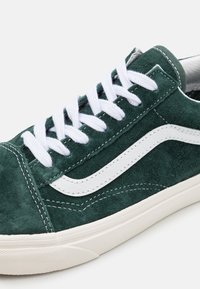 Grüner Wildledersneaker mit weißen Schnürsenkeln, einem weißen Seitenstreifen und kontrastierenden Nähten, einem strukturierten Obermaterial und einer Gummisohle.
