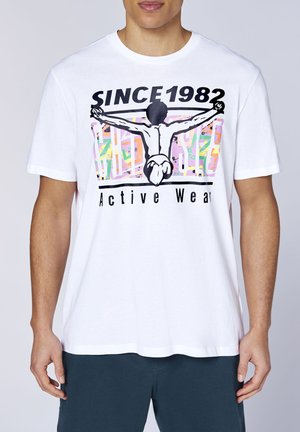 Mann trägt weißes T-Shirt mit Grafik einer Person, die die Arme weit ausstreckt, Text "SINCE 1982" und "Active Wear" vorne.