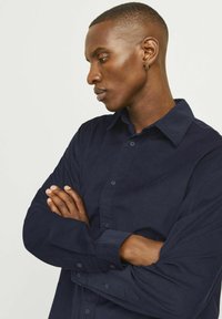 Camicia in corduroy blu navy con maniche lunghe, patta di bottoni e colletto strutturato. Presenta un tessuto testurizzato e un design dal taglio rilassato.