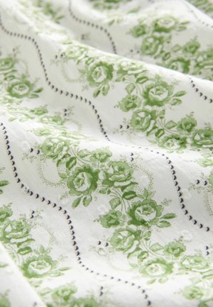 Cotton fabric featuring a green floral pattern on a white background, with stitched lines and swirls for added texture and detail.