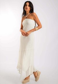 Vestido maxi blanco sin mangas con un patrón texturizado, dobladillo acampanado y un diseño en capas. Llevado con cuñas de esparto en color tostado para crear contraste.