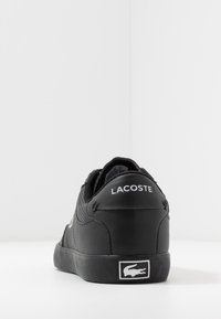 Baskets noires avec un matériau texturé, talon arrondi et logo Lacoste blanc à l'arrière. Comprend une semelle en caoutchouc et des accents cousus.