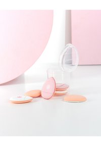 Makeupapplicatorer i olika former, inklusive en rosa ägg med vita accenter, förvarade i en transparent behållare på en vit yta.