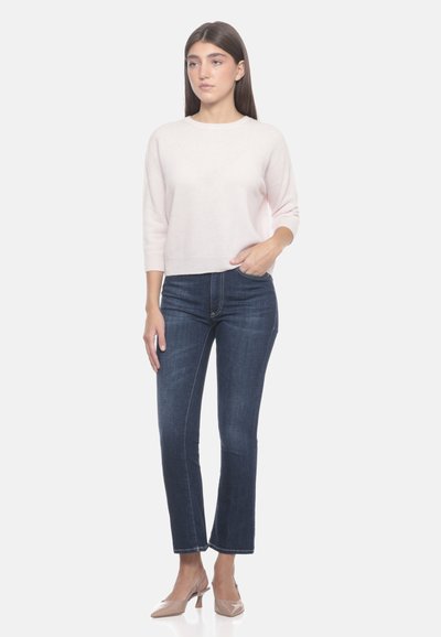 Maglione rosa chiaro con maniche a tre quarti, abbinato a jeans dritti blu scuro e scarpe con tacco beige. Texture complessivamente liscia.