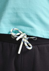 Turquoise t-shirt met een ronde zoom, gecombineerd met zwarte joggingbroek met een wit en blauw gestreepte trekkoord en plastic uiteinden.