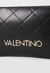 Černá kožená peněženka s prošívaným vzorem, na přední straně s zlatým logem "VALENTINO". Hladký povrch s tónovým prošíváním.