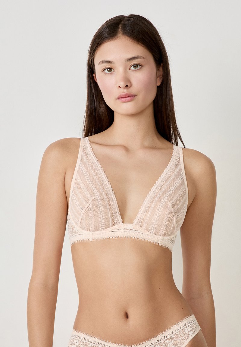 Kanten bralette in zacht perzik, met een diepe V-halslijn, ingewikkelde gestreepte patronen, gegolfde randen en dunne verstelbare bandjes.