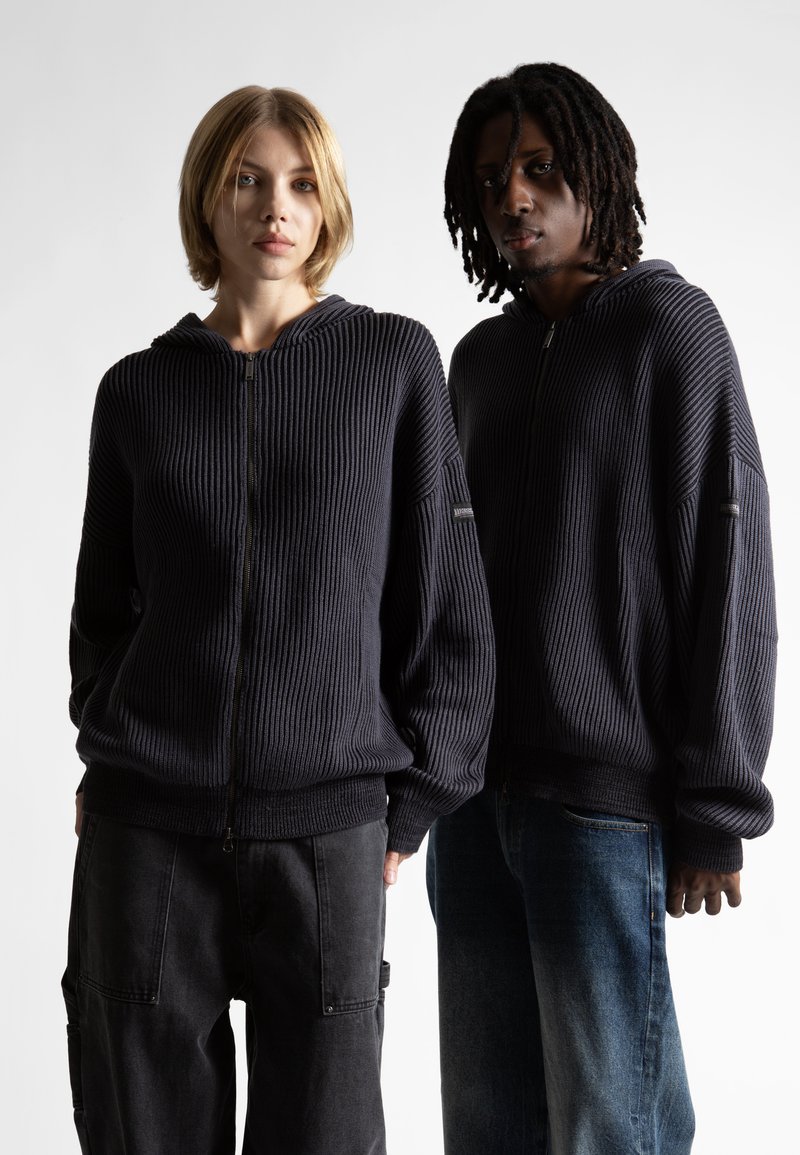 Hanorace cu glugă, de culoare bleumarin, cu textura ribbed, dotate cu fermoar frontal și croială oversized, asortate cu pantaloni din material închis și pantaloni din denim deschis.