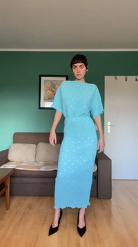 Vestido midi azul claro com mangas curtas e soltas, tecido texturizado e padrão de pontos prateados. Usado com saltos pretos pontiagudos.