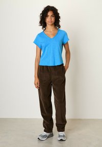 Modra kratka majica s V-izrezom v kombinaciji s svetlo rjavimi žametnimi hlačami. Obleka ima sproščen design in mehak otip.