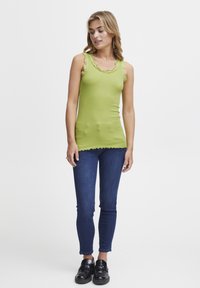 Roheline tank top, mille ääres on sklefta lace trim, kihisev disain, koos tume siniste kitsaste teksade ja mustade libisemisjalanõudega. Lihtne ja lõdvestunud välimus.