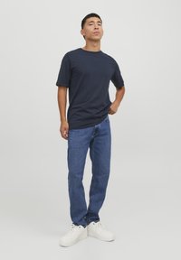 Marineblå t-skjorte med kort erm, avslappet passform, kombinert med lyseblå denimjeans og hvite joggesko. Enkelt design, glatt tekstur.