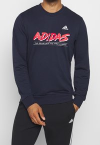 Felpa a maniche lunghe blu navy con logo "ADIDAS" bianco e rosso, scollatura tonda, polsini e fondo a costine, materiale misto cotone.