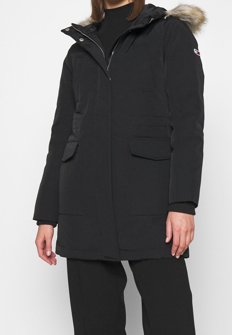 Zwarte geïsoleerde parka met een met bont gevoerde capuchon, voorkant met rits, meerdere zakken en ribgebreide manchetten. Gladde textuur en recht gesneden ontwerp.