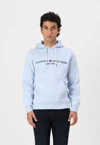 Γαλάζια hoodie με μπροστινή τσέπη, κορδόνια και λογότυπο "TOMMY HILFIGER EST. 1985". Λεπτομέρειες με ριμπ μανσέτες και στρίφωμα, βαμβακερό υλικό.