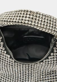 Mustan tõmblukuga kott, kaunistatud hõbedaste rhinestone'idega. Sisemine vooder on musta kangaga, millel on kaubamärgi silt.