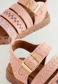 rosa tygsandaler med tre justerbara remmar, gyllene spännen och dekorativ broderi med geometriska mönster. Brun texturerad sula.