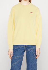 Sudadera amarillo de cuello redondo hecha de una tela suave, con un pequeño logo rojo de Levi's en el pecho y puños y dobladillo de canalé.