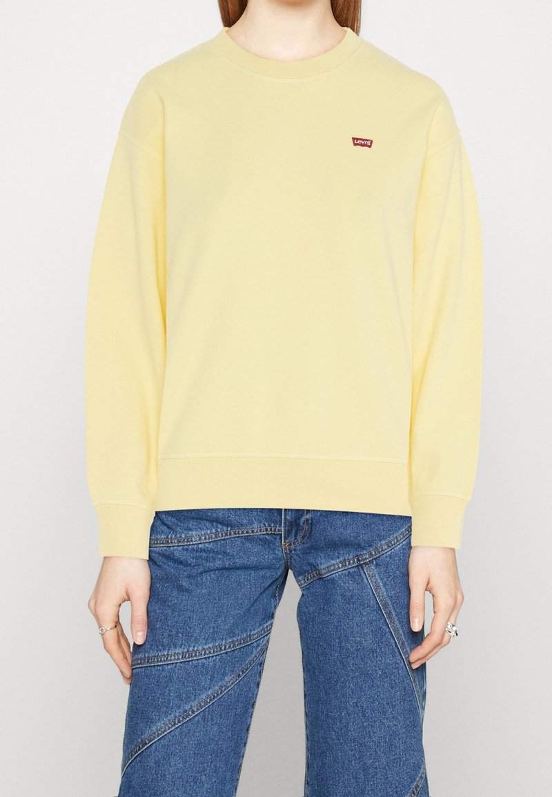 Sudadera amarillo de cuello redondo hecha de una tela suave, con un pequeño logo rojo de Levi's en el pecho y puños y dobladillo de canalé.