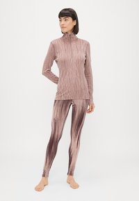 Camisola leve de mangas compridas e leggings em tons de rosa com um padrão de riscas diagonais texturizadas. A camisola tem um colar alto e fecho éclair.