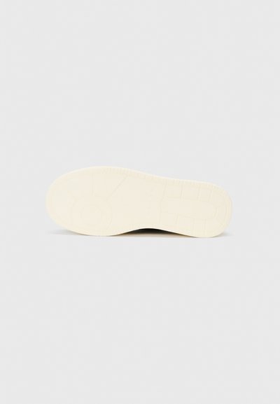 Sole of a sneaker in off-white rubber, featuring a textured grip pattern and circular design element. Smooth finish with subtle detailing.
