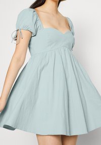 Ljusblå klänning med en figursydd överdel och hjärtformad urringning, som vidgar sig från midjan med en mjuk textur och puffärmar.