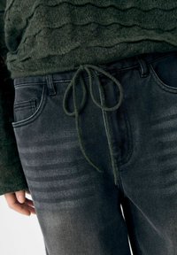Zwarte denim jeans hebben een koord in de taille, voorzakken en een gestructureerde, gewassen afwerking met een geleidelijke kleurverloop.