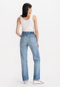 Jeans de tiro alto en azul claro con un corte relajado, que presentan bolsillos y una etiqueta de cuero negro en la parte posterior. Combinados con una camiseta sin mangas blanca.