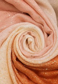 Tessuto morbido in sfumature degradé di pesca, crema e arancione, con scaglie di metallo dorato sparse, arrotolato a spirale.