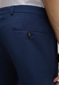Marineblaue Hosen aus strukturiertem Stoff mit einer Gesäßtasche mit Knopfverschluss. Das Design beinhaltet eine flache Vorderseite und eine taillierte Passform.