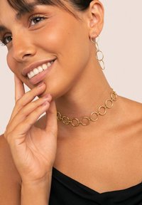 Choker de cadena circular dorada y pendientes a juego. Metal liso y brillante con eslabones grandes y pequeños alternos, usado sobre una blusa oscura.