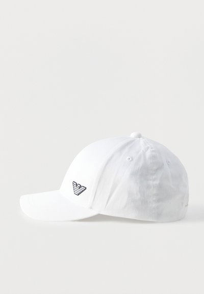 Valge puuvillane pesapallimüts kõvera äärisega, mille esimesel vasakul paneelil on väike must-valge triibuline kotka logo.