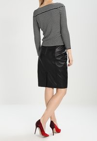 Gonna a tubino in pelle nera abbinata a una maglietta a maniche lunghe bianco e nera a righe e scarpe con tacco rosse. La vista posteriore mette in evidenza il design aderente.