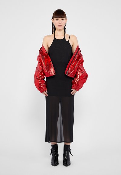 Black sheer dress layered under a shiny red cropped jacket with textured finishing; styled with black ankle boots and long earrings.
