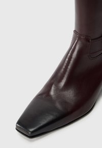Bottines en cuir bourgogne à bout carré, au design épuré et aux coutures minimales, avec une texture lisse et un accent noir au niveau du bout.