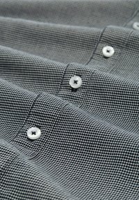 Camisa de botones gris con un patrón de cuadrícula texturizado. Presenta botones blancos y una superficie de tela lisa.