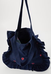 Denim auduma soma ar kraukšķīgiem malām, tumši zila krāsa un izšūtas sarkanas sirds. Aprīkota ar diviem izturīgiem rokturiem nēsāšanai. Atvērta augšdaļa.