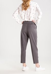 Szare dopasowane spodnie o skróconym kroju, z bocznymi kieszeniami i gładką fakturą. W połączeniu z białą koszulą z guzikami, ozdobioną subtelnym wzorem ptaków.