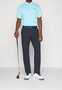 Jasnoniebieska koszulka polo z krótkim rękawem, ciemnoszare spodnie, niebieski pasek i białe buty golfowe, trzymający kij golfowy.