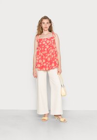 Top de tanque floral vermelho com alças ajustáveis, combinado com calças largas brancas, sandálias de salto amarelas e uma pequena bolsa amarela.