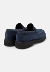 Navy suede loafers with a rounded toe, slip-on design, padded collar, and a textured black rubber sole. Subtle branding on the heel.