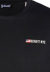 Camiseta de algodón negra con cuello redondo y mangas cortas. En el frontal muestra "SCHOTT NYC" en texto blanco y un pequeño icono de la bandera americana.
