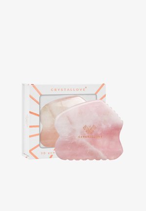 3D kryształowy kamień wykonany z polerowanego różowego kryształu o zaokrąglonych krawędziach, z logo w kolorze złotym na powierzchni, zaprezentowany w pudełku o geometrycznym wzorze.